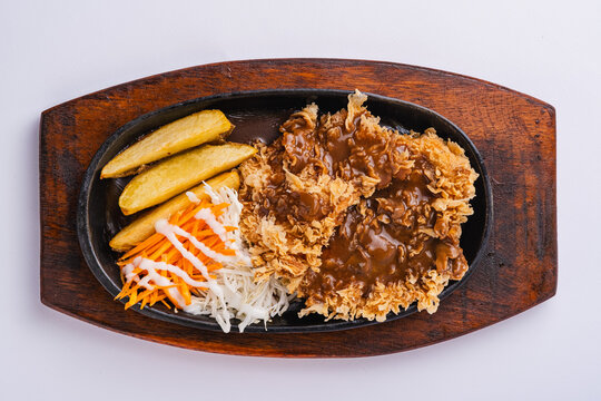 chicken steak served on a hot plate sprinkled with barbaque sauce accompanied by fries, cabbage and carrots with a little added mayonnaise, and surrounded by a white background