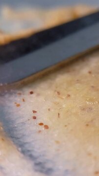 Extreme close up of spreading skin cream with a shiny metal tool applicator. Detailed macro shot of cosmetic product texture and smooth consistency being swiped evenly.