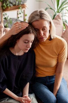 Caring mother sitting beside troubled teenage daughter on sofa, parent lovingly comforting unhappy teen girl creating moment of care, mom with child together