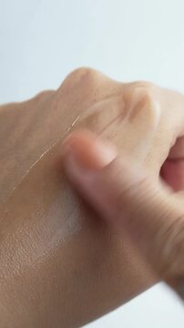 Applying moisturizing skin cream onto back of hand with finger. Close up of beauty skincare cosmetic routine on white background.