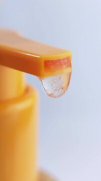 Clear liquid coming out and dripping from orange product packaging. Vertical close up on white background. Beauty concept for skincare.