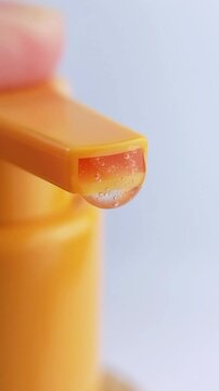 Close up of clear liquid inside orange cosmetic tube not dispensing. Skincare packaging concept in vertical view.