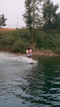 Vertical video: Riding helmeted rider being pulled by cable at park hitting ramp for jump, landing