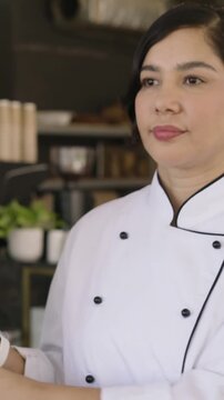 Vertical video: Touching doorframe, chef in white coat composing in cafe kitchen, preparing to work