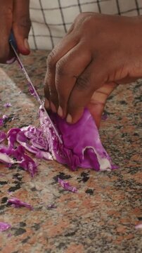 Vertical video: Placing wedge, cook hands slicing purple cabbage on counter into bowl with knife