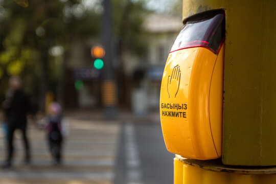 Yellow touch sensor button at a crosswalk with Kazakh and Russian text. Almaty, Kazakhstan - September 30, 2024
