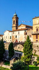 Fototapeta premium A picturesque view of an old town with a church tower, stone bridge, and lush greenery on a clear day