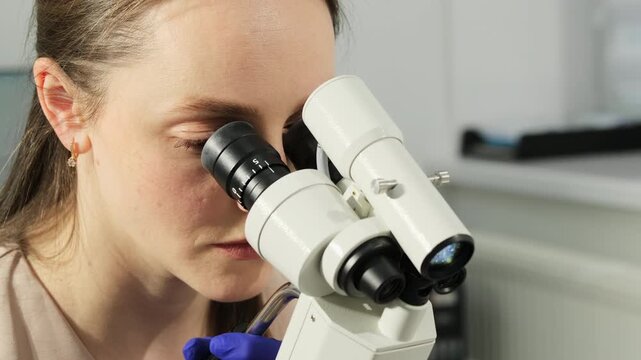 Doctor reviews cervical sample with microscope during Pap test procedure. Specialist focuses optics precisely inspecting specimen step by step