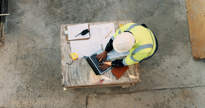 Typing, laptop and above of man on construction site for planning, building permit and compliance. Architecture, documents and person on computer for renovation, online blueprint and infrastructure
