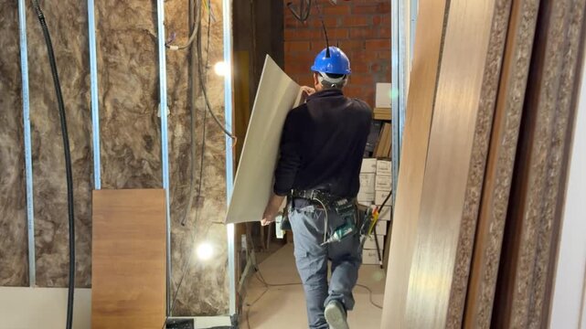 Construction worker carrying drywall sheet at building site