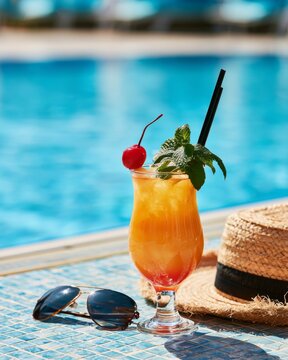 Tropical poolside cocktail with straw hat and sunglasses for luxury summer vacation