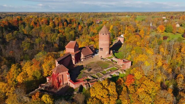 Drone lowers above Turaida Castle surrounded by golden Gauja Valley forests.