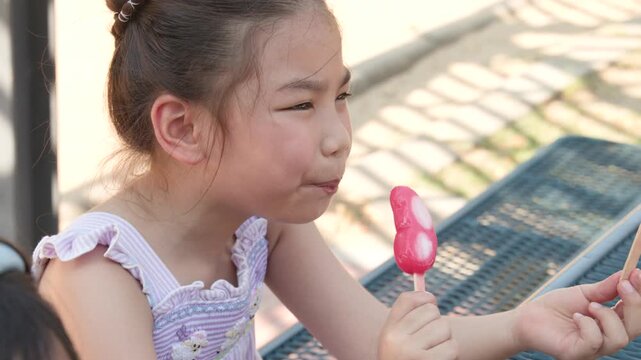 Young Asian Girl Eating a Pink Butterfly Popsicle in a Sunny Park