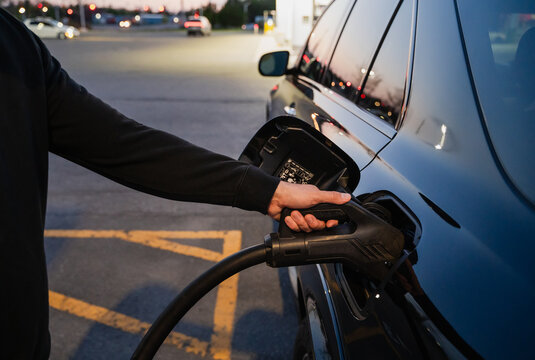 Close up of a man plugging in charger to electric car at night