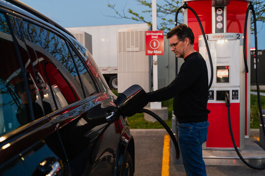 Man charging electric vehicle at dusk at public charging station.