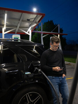 Man browsing phone while charging his electric car at night