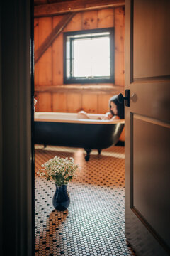 Woman relaxing in rustic bathroom with clawfoot bathtub