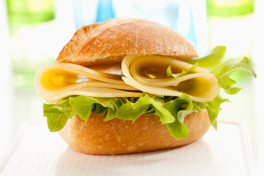 Bread roll with Emmentaler cheese on chopping board, close up