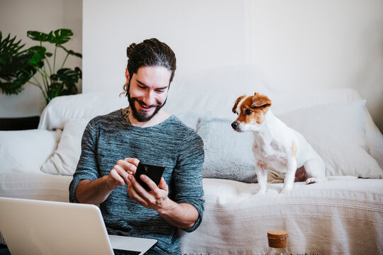 Man with laptop using mobile phone while sitting by dog at home