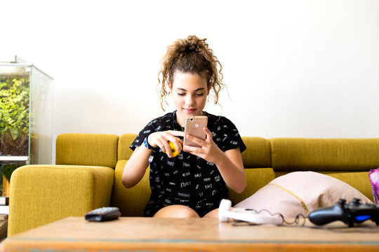 Portrait of girl sitting on the couch at home using smartphone