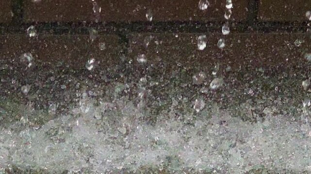 水しぶきや水滴のある流れる噴水　レンガの壁を噴出される水がはじける風景　クローズアップ