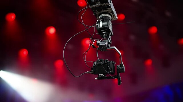 Professional gimbal camera mounted on overhead rig for stage lighting filming.
