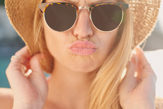Kiss, sunglasses and travel with woman outdoor for getaway, holiday or vacation in summer. Hat, shades and sunshine with person pouting at beach for coastal trip, weekend or wellness as tourist