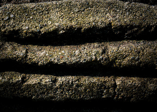 Rugged stone steps show weathered texture and deep shadows. Each surface bears moss and grit, hinting at age and neglect. Dark crevices frame the stones, emphasizing their ancient presence