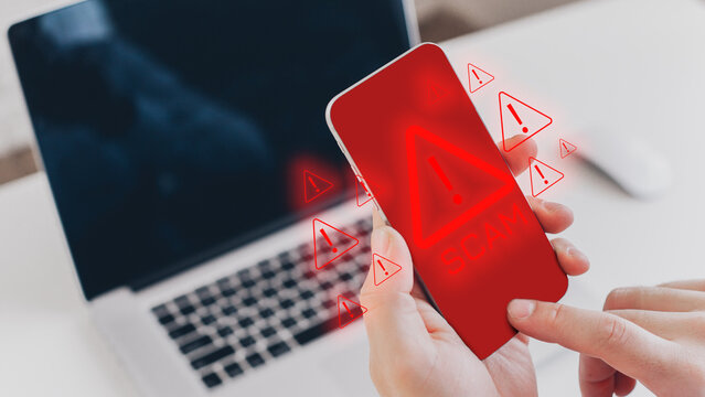 Message shows scam warning on phone screen near laptop during daytime