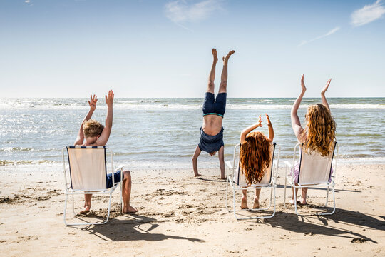 Netherlands, Zandvoort, family clapping hands for father doing a handstand on the beach