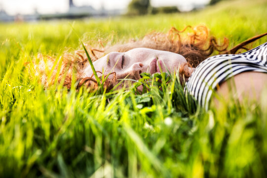Portrait of redheaded young woman with eyes closed lying on meadow