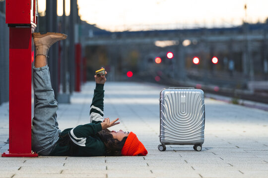 Girl talking selfie through smart phone lying down at train platform