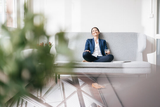 Smiling businesswoman sitting on couch with beverage