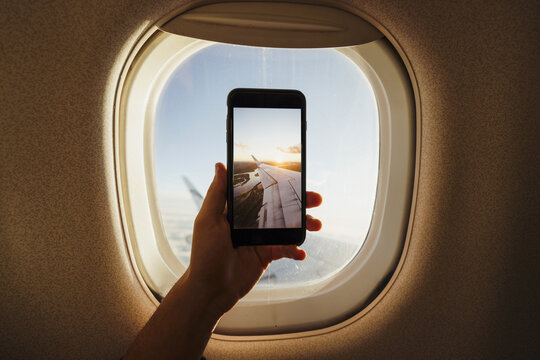 Hand taking cell phone picture out of plane window
