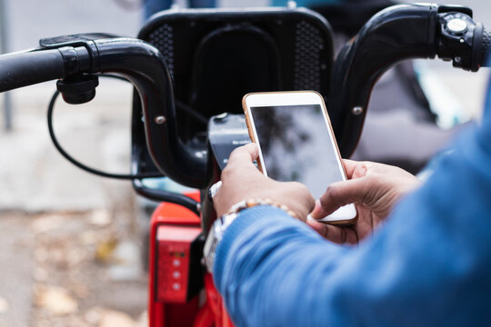 Hands of man using smart phone for renting bicycle at parking station