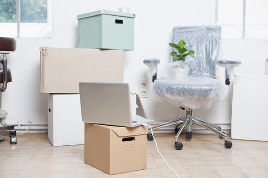 Stack of cardboard boxes, wrapped swivel chair and a notebook in an office