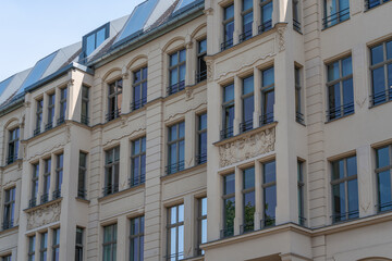 Fototapeta premium A restored residential facade shows tall windows and decorative stucco. Modern roof glazing and cream walls blend historic detail with urban renewal.
