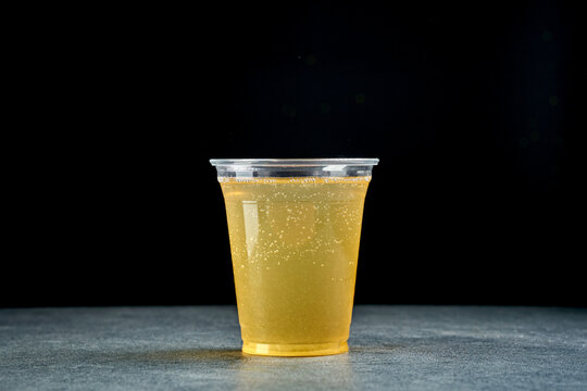 Refreshing carbonated lemonade drink in clear plastic takeaway cup with gas bubbles, side view of cold fizzy citrus beverage on dark background, fast food beverage delivery concept