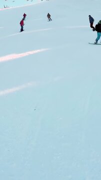 Vertical video: Lift unloading as snowboarder in pink jacket carving toward lens on slope to slow