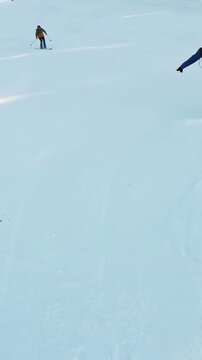 Vertical video: Carving female boarder purple jacket down ski run as group starts, lift, copy space