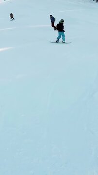 Vertical video: Starting descent sending boarder in teal pants carving down ski run to follow group
