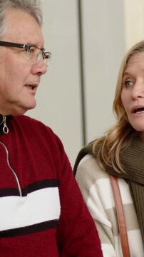 Vertical video: Turning head, talking mature man starting chat with woman in lobby, in red sweater