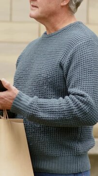 Vertical video: Peering at phone, senior with glasses tapping, looking up to scan steps holding bag