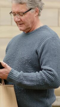 Vertical video: Phone buzzing, man in blue sweater scrolling it in lobby, lifting head, holding bag