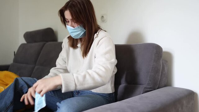 Young woman wearing protective face mask at home while preparing extra medical mask during seasonal virus outbreak healthcare safety and infection prevention concept