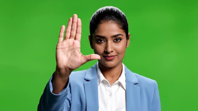 Young woman in white shirt and tie making stop gesture against green background hand