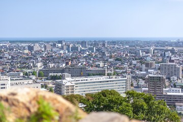 Obraz premium 米子城跡の天守台から手前の石垣越しに一望する米子市街地と日本海の水平線/Panoramic View of Yonago Cityscape and the Horizon of the Sea of Japan Beyond the Foreground Stone Walls from the Tenshudai of Yonago Castle Ruins