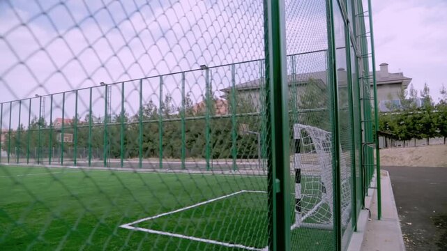 Tashkent, Uzbekistan - 06 06 2025: Empty fenced soccer field with bench on cloudy day