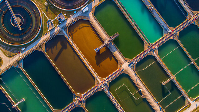 Aerial view of a wastewater treatment plant with colorful rectangular sedimentation tanks and circular clarifiers in a facility