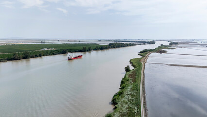 Fototapeta premium Cargo ship navigating Guadalquivir river through fields
